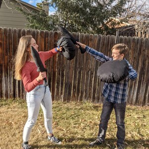 May include: Two black fabric swords and two black circular fabric shields. The swords have a simple hilt and blade design, while the shields are round and padded. These soft play items are constructed from solid black textile material throughout.