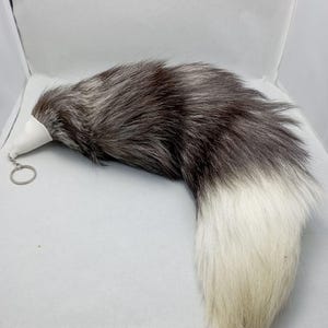 May include: A silver and white faux fur tail with a key ring attached. The tail is about 12 inches long and is made of soft, fluffy fur.