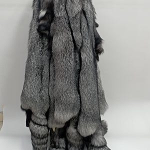 Puede incluir: Un conjunto de pieles de zorro plateado con puntas blancas. Las pieles están dispuestas en una pila vertical con las colas colgando.