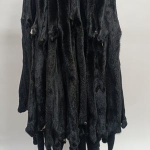 May include: A group of black mink fur pelts hanging on a white wall. The pelts are arranged in rows and are all the same size.