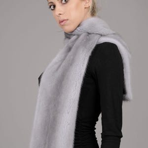 May include: A light gray fur scarf worn around the neck of a person wearing a black shirt.