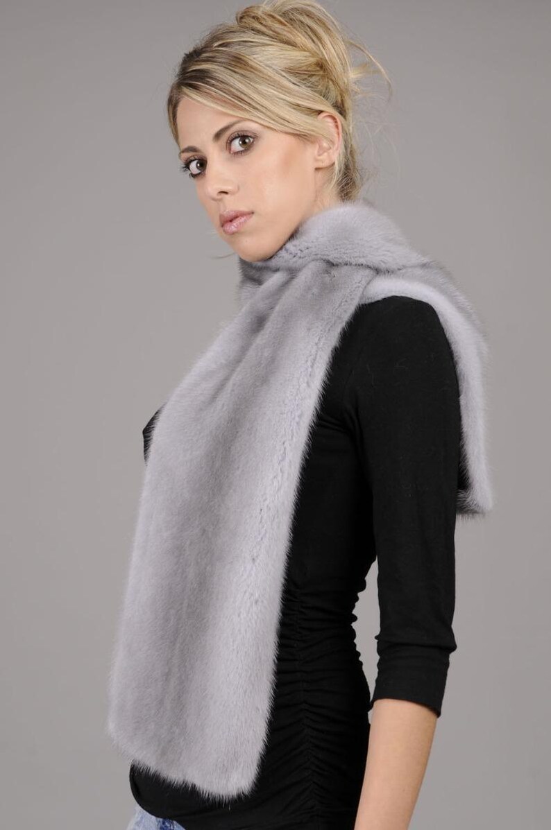 May include: A light gray fur scarf worn around the neck of a person wearing a black shirt.