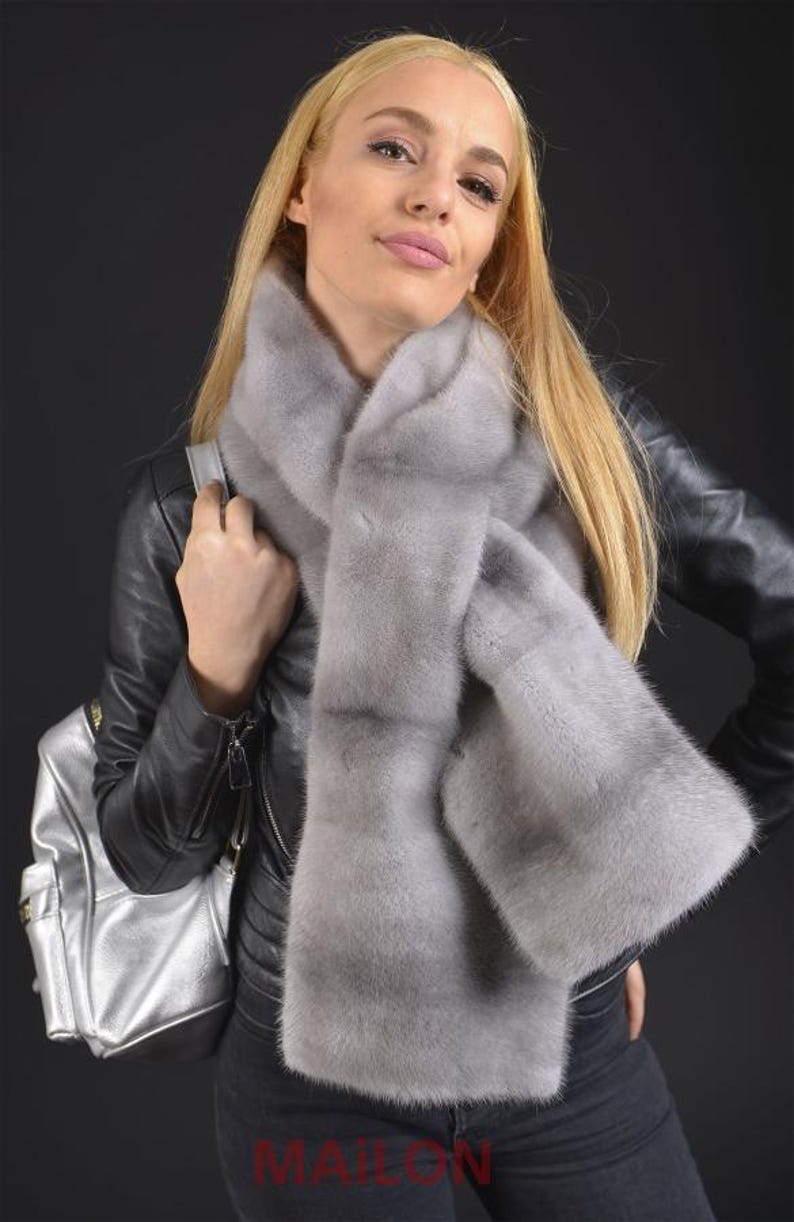 Puede incluir: Una bufanda de piel gris claro con un dise&ntilde;o largo y fluido. La bufanda la lleva una persona con el pelo largo y rubio y est&aacute; drapeada alrededor del cuello.