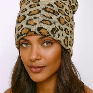 May include: A beige beanie with a leopard print pattern in shades of brown and black. The hat is made of a soft, knitted material. The beanie is a stylish accessory for cold weather.