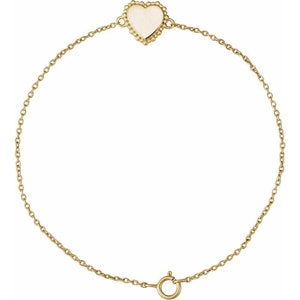 May include: A delicate gold chain bracelet with a small white heart charm. The heart has a beaded border.
