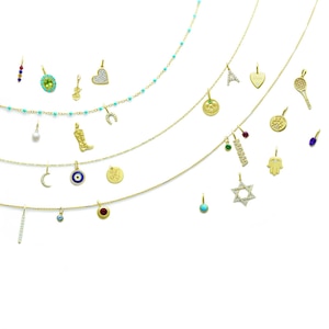 Puede incluir: Collares de oro con varios colgantes, incluyendo un corazón, una raqueta de tenis, una estrella y una herradura. Algunos colgantes están adornados con piedras preciosas. Un collar presenta cuentas turquesas. Los colgantes cuelgan de delicadas cadenas de oro.