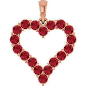 May include: A heart-shaped pendant crafted from rose-toned metal, featuring a series of round, deep red faceted stones set in a continuous border. The design includes a single bail at the top for attachment, creating a symmetrical open-center frame.