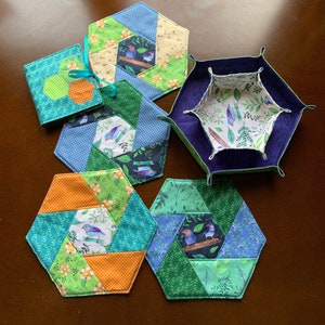 Pode incluir: Seis  tapetes hexagonais de tecido com um design de patchwork que apresenta tecidos verdes, azuis, laranjas e amarelos com uma estampa de pássaros. Os tapetes são feitos de tecido e têm um design acolchoado.