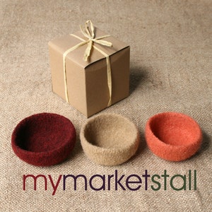 May include: Three felt bowls in burgundy, tan, and orange, with a small gift box tied with raffia. The bowls are arranged on a textured, neutral-toned surface. The text "mymarketstall" is visible.