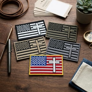 May include: A collection of embroidered patches featuring the American flag with a Christian cross design. The patches come in various color schemes, including black and white, olive green, tan, and gray. The patches are rectangular and have a stitched border.