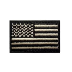 May include: A rectangular embroidered patch featuring a stylized United States flag design. The patch is rendered in a monochromatic black and off-white color scheme, with the stars and stripes clearly defined by dense, textured thread stitching.