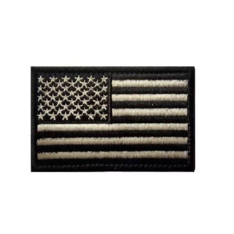 May include: A rectangular embroidered patch featuring a stylized United States flag design. The patch is rendered in a monochromatic black and off-white color scheme, with the stars and stripes clearly defined by dense, textured thread stitching.
