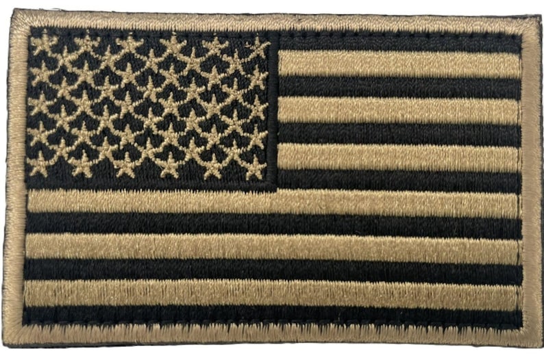 May include: A rectangular embroidered patch featuring a stylized United States flag design. The pattern consists of alternating horizontal black and tan stripes, with a field of tan stars on a black background in the upper left corner.