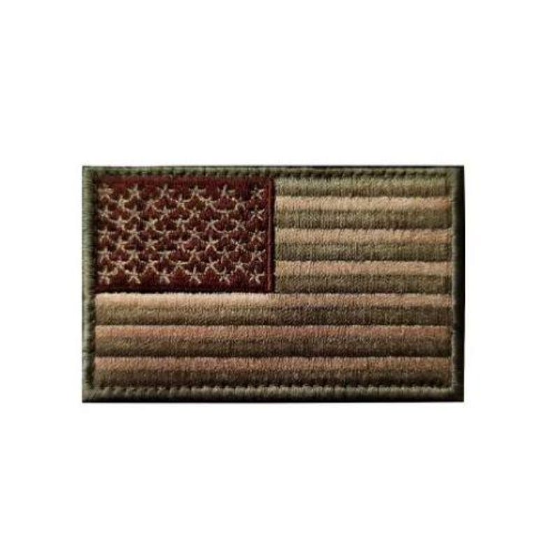 May include: A rectangular embroidered patch featuring the United States flag in a muted, monochromatic olive green and brown color scheme. The design includes the traditional star field and horizontal stripes, all rendered with detailed stitching.
