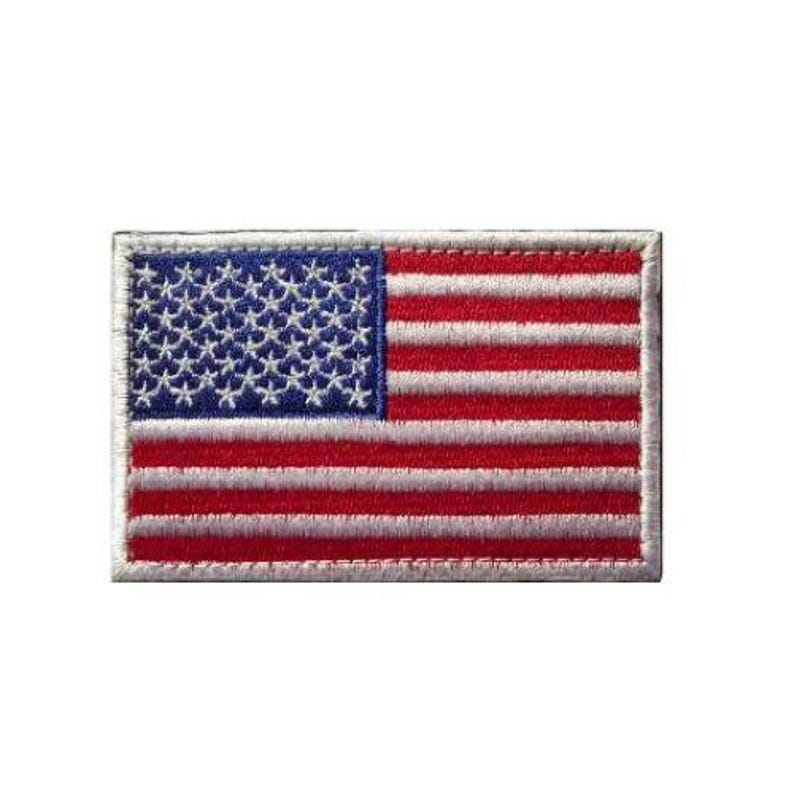 May include: A rectangular embroidered patch featuring the flag of the United States of America. The design includes a blue canton with white stars on the left and alternating horizontal red and white stripes across the rest of the fabric surface.