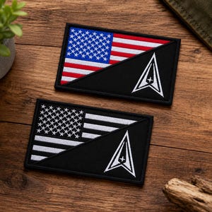 May include: Two rectangular embroidered patches featuring a diagonal split design. One patch displays the American flag in red, white, and blue, while the other shows a black and white American flag. Both feature a white delta-shaped emblem.