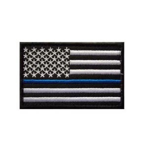 May include: A rectangular embroidered patch featuring a stylized American flag design. The flag is rendered in black with white embroidered stars and horizontal stripes, accented by a single horizontal blue stripe across the center.