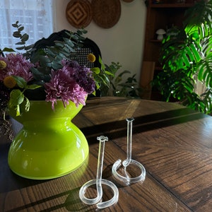 May include: Two clear glass ring holders with a spiral design. The holders are on a dark wood table.