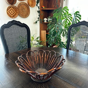 May include: A brown woven bamboo basket with a circular base and a wide, shallow bowl. The basket is sitting on a dark wood table.