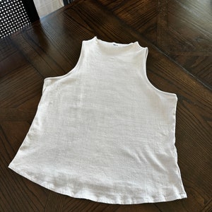 K&ouml;nnte beinhalten: Ein wei&szlig;es &auml;rmelloses geripptes Tanktop mit einem Stehkragen.
