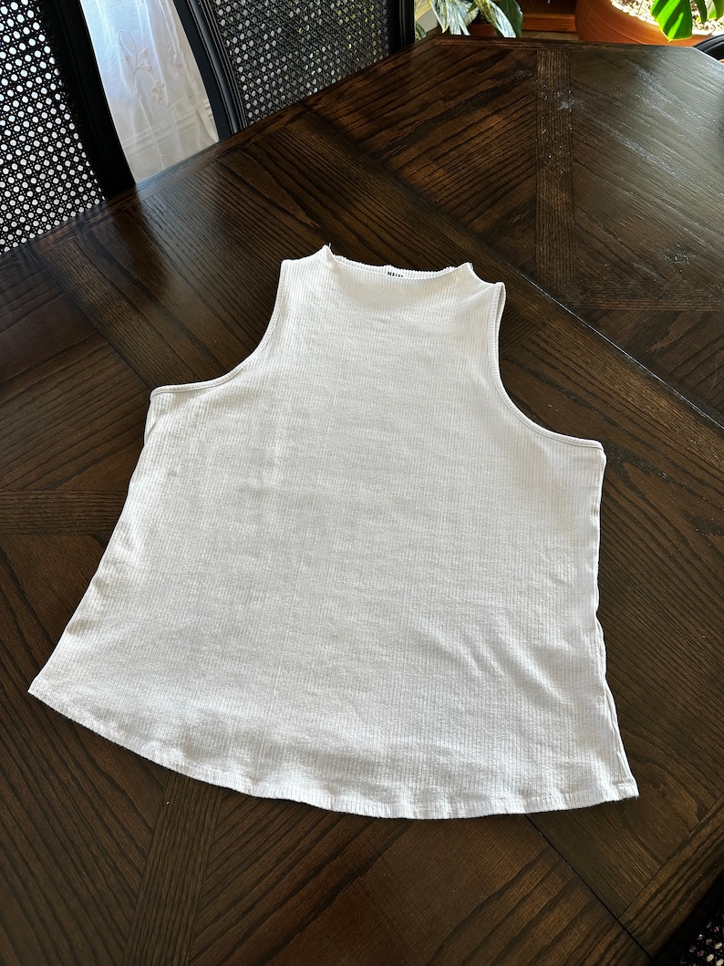K&ouml;nnte beinhalten: Ein wei&szlig;es &auml;rmelloses geripptes Tanktop mit einem Stehkragen.