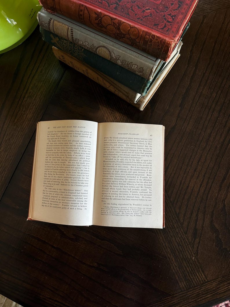 May include: An open book with a brown leather cover. The book is titled "The Rise and Fall of the Nation" and "Benjamin Franklin". The text on the pages discusses the history of the American Revolution.