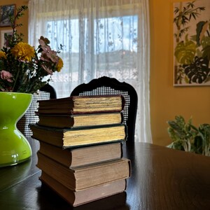 May include: A stack of five vintage hardcover books with brown, gold, and red covers sits on a dark wooden table. The books are arranged in a neat pile, with the spines facing out.