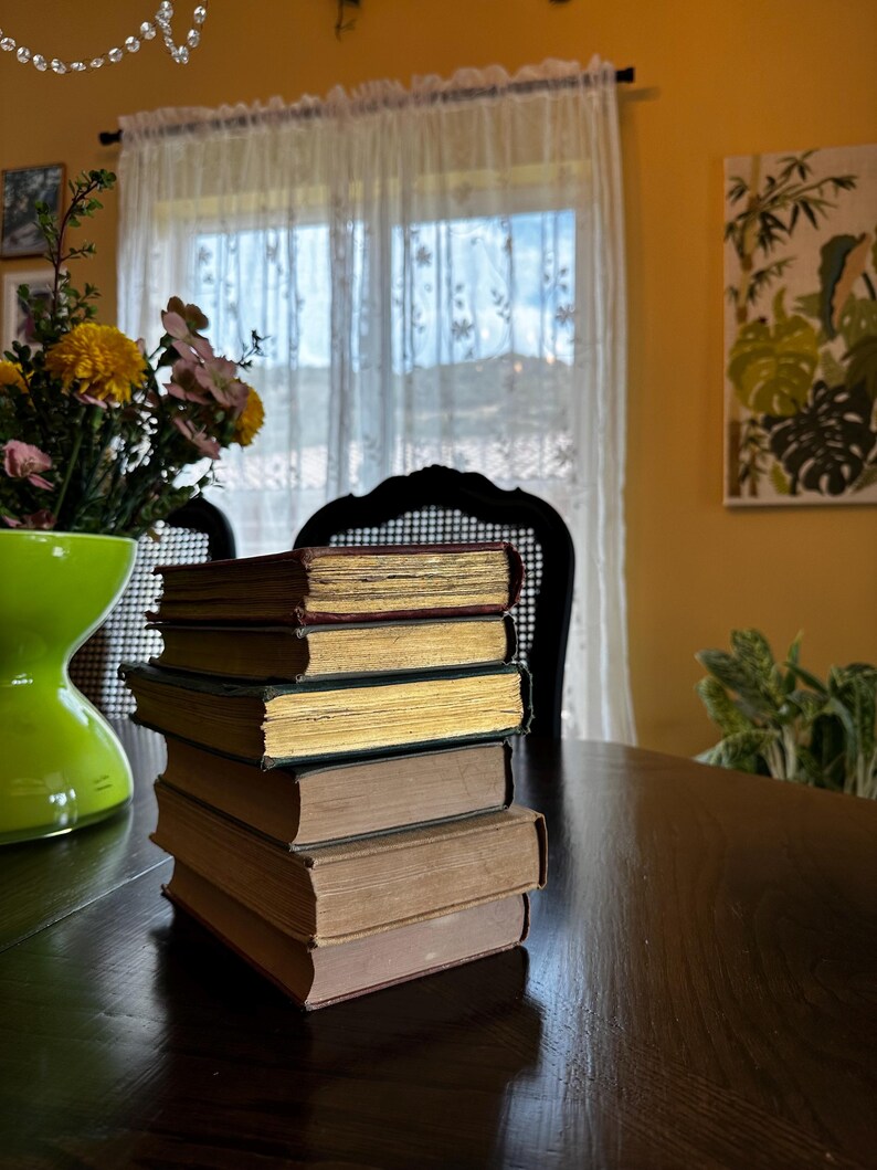 May include: A stack of five vintage hardcover books with brown, gold, and red covers sits on a dark wooden table. The books are arranged in a neat pile, with the spines facing out.
