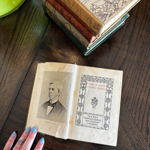 May include: An open book with a portrait of Oliver Wendell Holmes on the left page and the title "Poems of Oliver Wendell Holmes" on the right page. The book is published by Thomas Y. Crowell and Company, Publishers, New York.