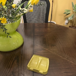 May include: A yellow plastic spoon rest with two slots on a dark wood table.