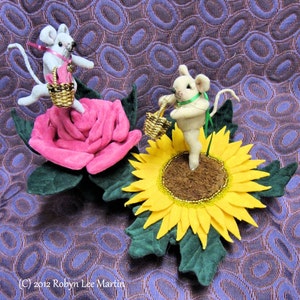 May include: Two felt mice with baskets sit on a pink rose and a yellow sunflower. The flowers have green leaves, set against a patterned purple fabric. The image is signed by the artist, Robyn Lee Martin, with the year 2012.