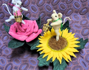 May include: Two whimsical felt mice, each carrying a tiny basket, are perched atop a large pink rose and a yellow sunflower. The flowers have green leaves, and the background is a patterned purple fabric. The image is signed by the artist.