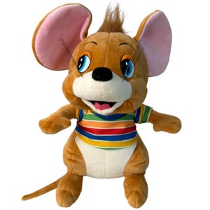 May include: A plush toy of Jerry Mouse from Tom and Jerry. The toy mouse has brown fur, large pink-lined ears, and blue eyes. He wears a striped shirt with rainbow colors. The toy is standing with its arms outstretched.