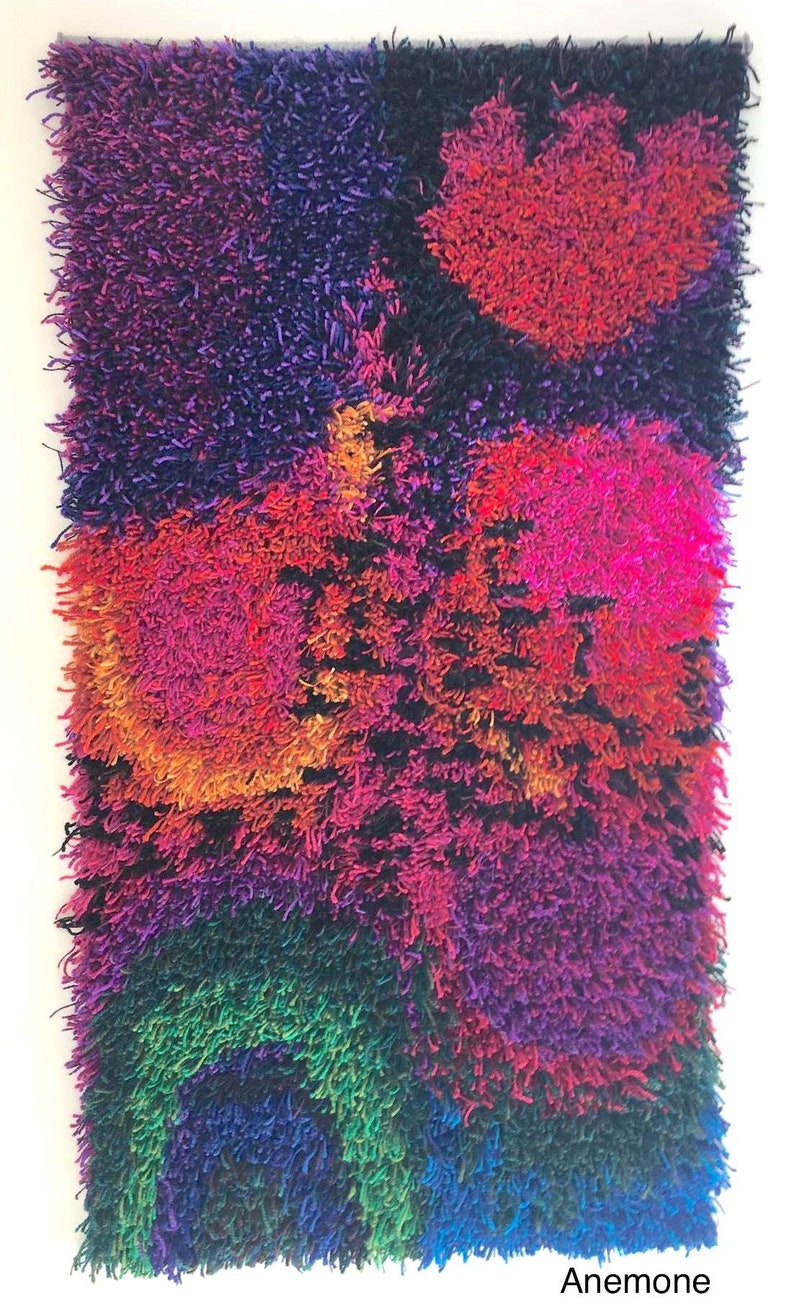 May include: A rectangular, shaggy textile art piece with a vibrant color palette. The artwork features a mix of colors, including red, pink, orange, purple, green, and blue. The word "Anemone" is printed at the bottom.