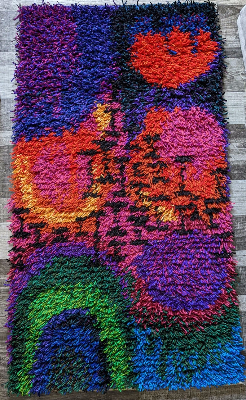 May include: A vibrant, rectangular shag rug with a colorful abstract design. The rug features a mix of colors, including red, pink, purple, green, and blue. The texture is thick and shaggy, creating a cozy and visually appealing piece.