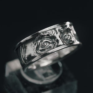 Könnte beinhalten: Ein silberner Ring mit einem detaillierten Design von zwei Augen auf der Band.