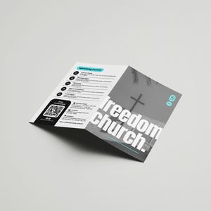 Op de afbeelding: Een drievoudig gevouwen brochure voor Freedom Church. De voorzijde toont een zwart-witfoto van een kruis tegen een bewolkte lucht. De tekst "Freedom Church." staat in witte letters met een turquoise onderstreping. De achterzijde bevat een QR-code en een lijst met aankomende evenementen.