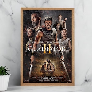 May include: A framed poster for the film "Gladiator II", featuring actors Paul Mescal, Pedro Pascal, Connie Nielsen, and Denzel Washington. The poster has a dark, action-packed design with the title "Gladiator II" and the words "Coming Soon" at the bottom.