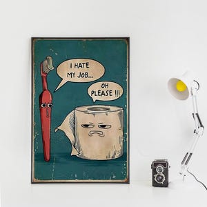 May include: A framed poster with a teal background features cartoon illustrations of a red toothbrush and a roll of toilet paper with facial expressions. The toothbrush says, "I hate my job..." and the toilet paper replies, "Oh please!!!"