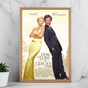 May include: A framed movie poster for "How to Lose a Guy in 10 Days" with Kate Hudson and Matthew McConaughey. The poster is in a light wood frame. The title is in red and white text. The actors are leaning against each other.