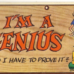 May include: A vintage wood sign with a cartoon illustration of a man reading a comic book. The sign says "I'm a Genius. Do I have to prove it?"
