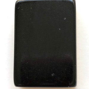 May include: A rectangular, solid black object with rounded corners. The surface has a glossy finish and minor imperfections. The object's shape is a simple rectangle, and it appears to be made of a solid, dark material.