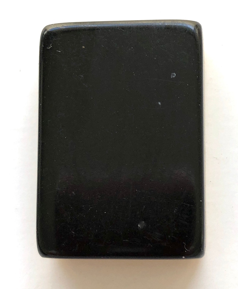 May include: A rectangular, solid black object with rounded corners. The surface has a glossy finish and minor imperfections. The object's shape is a simple rectangle, and it appears to be made of a solid, dark material.