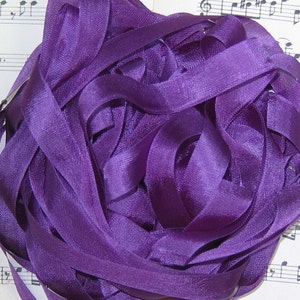 May include: A large pile of purple satin ribbon. The ribbon is arranged in a loose, tangled heap.