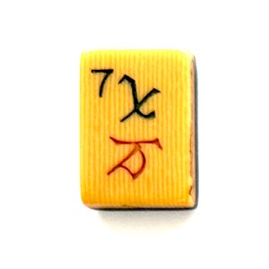 May include: A rectangular mahjong tile with a textured yellow surface. The tile features a black character in the upper left, a green character in the upper right, and a red character centered below them, all engraved into the yellow material.
