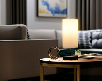 May include: A modern table lamp with a rectangular lampshade, sitting on a black base. A gold-colored decorative ring and a small potted plant are on the table. The table is brown with gold trim.