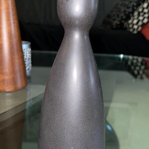 May include: A dark gray, speckled candle holder with a rounded base and a flared top. The candle holder has a smooth, metallic finish and a slender, elongated shape. The design is minimalist and modern, suitable for home decor.