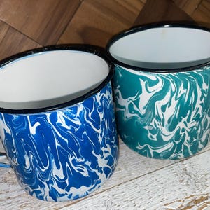 May include: Two enamel mugs with white and blue marbled designs. One mug is blue and white, the other is green and white.