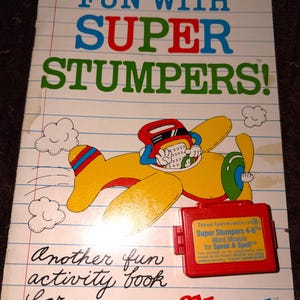 May include: A vintage "Fun With Super Stumpers" activity book for Speak & Spell. The cover features a yellow airplane with a pilot, clouds, and a red Texas Instruments Word Module. The book is designed for grades 4.5 and 6.