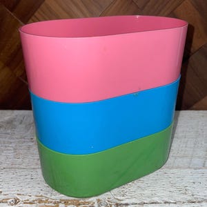 May include: A stack of three colorful plastic containers. The top container is pink, the middle is blue, and the bottom is green. The containers have a curved design and are stacked on top of each other.